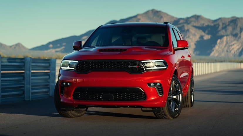 Red Dodge Durango SUV on an asphalt road at sunset with rugged mountains and a soft blue sky in the background.