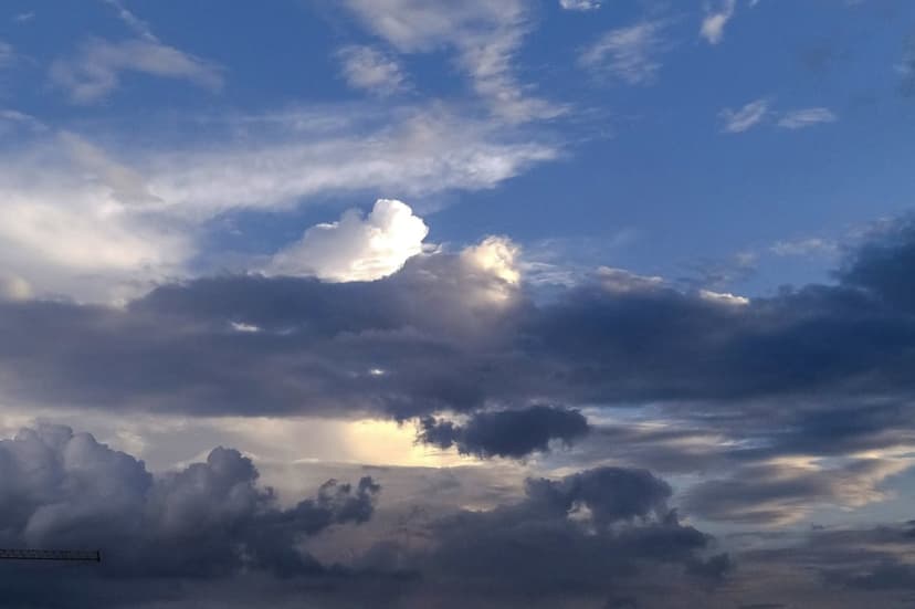 Golden sunbeams pierce through dark stormy cumulus clouds against a deep blue sky during a dramatic weather event.
