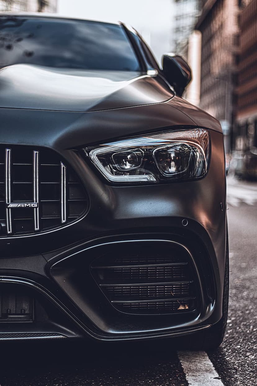 Mercedes-AMG GT front headlight and vertical slat grille on a wet asphalt street with urban reflections.