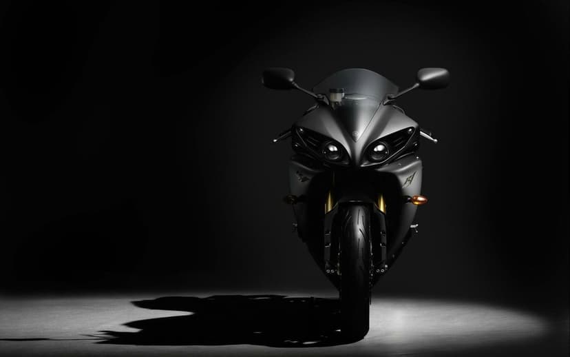 Front view of a matte gray Yamaha R1 motorcycle centered in a dark studio with dramatic spotlighting.