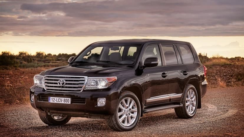 Black Toyota Land Cruiser SUV parked on a gravel path under a cloudy sunset sky with chrome accents and silver rims.