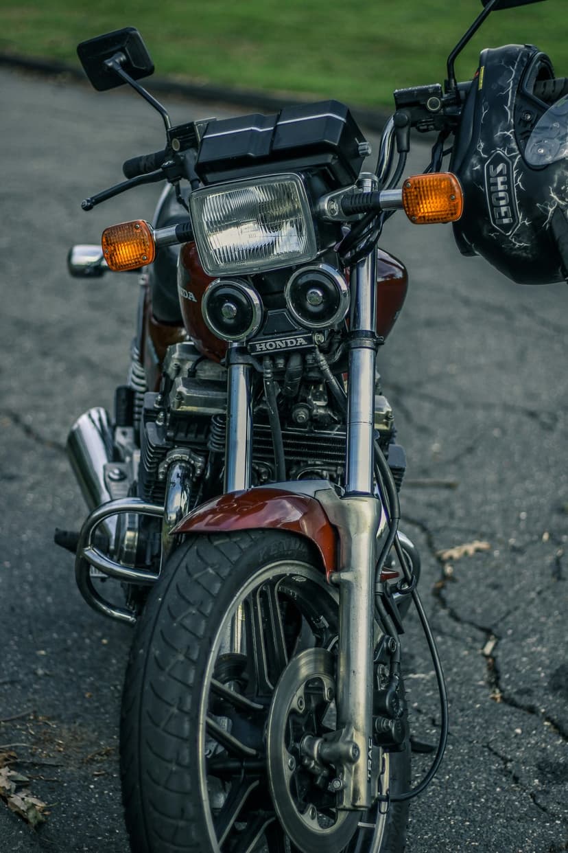 Dark red vintage Honda motorcycle with a large round headlight and black helmet hanging from chrome handlebars.