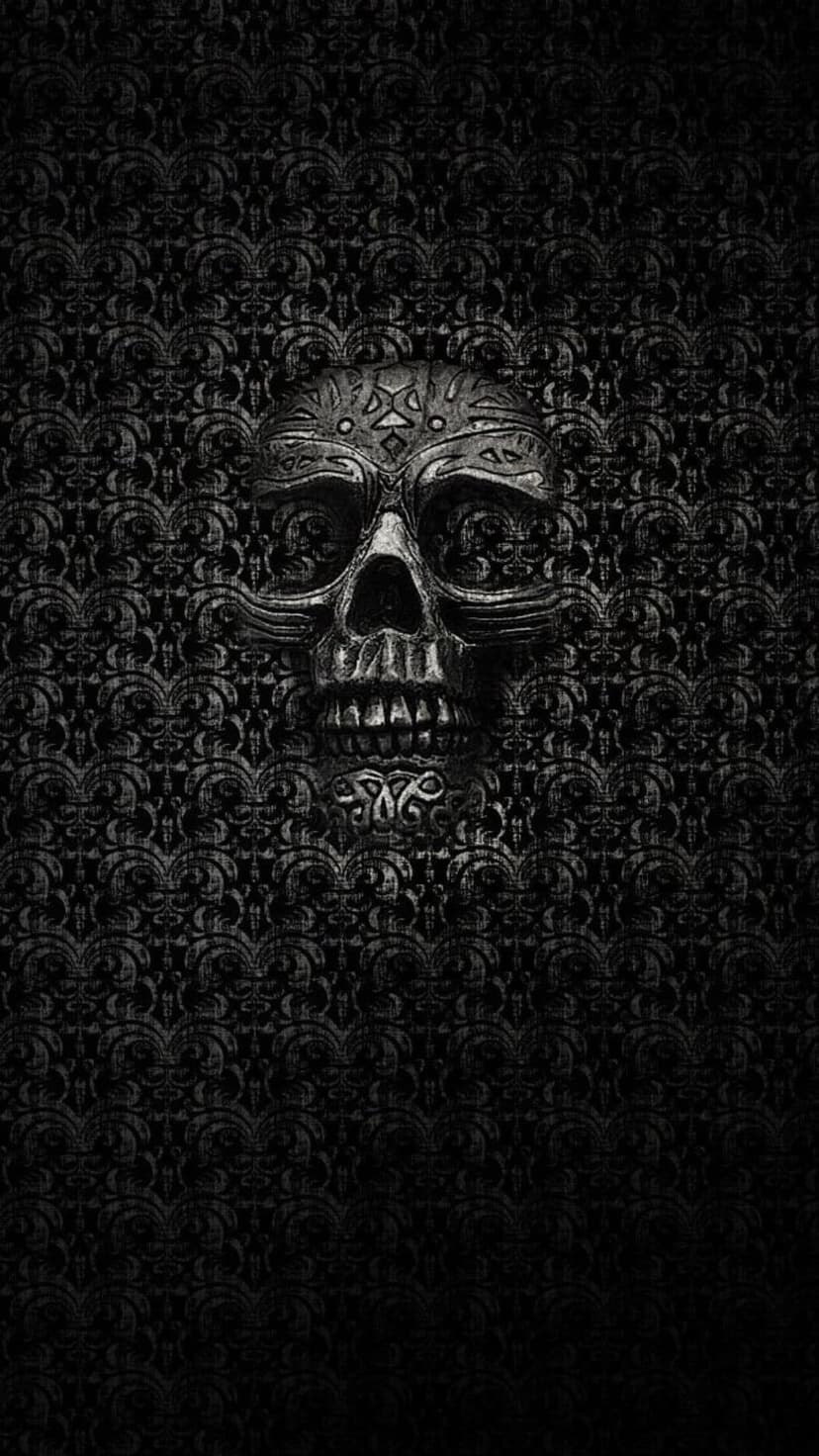 Metallic skull with star carvings positioned against a black textured damask wallpaper with floral motifs.