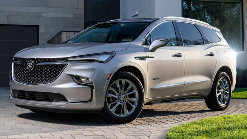 Silver Buick Enclave Avenir luxury SUV parked on a paved driveway with a modern architectural background.
