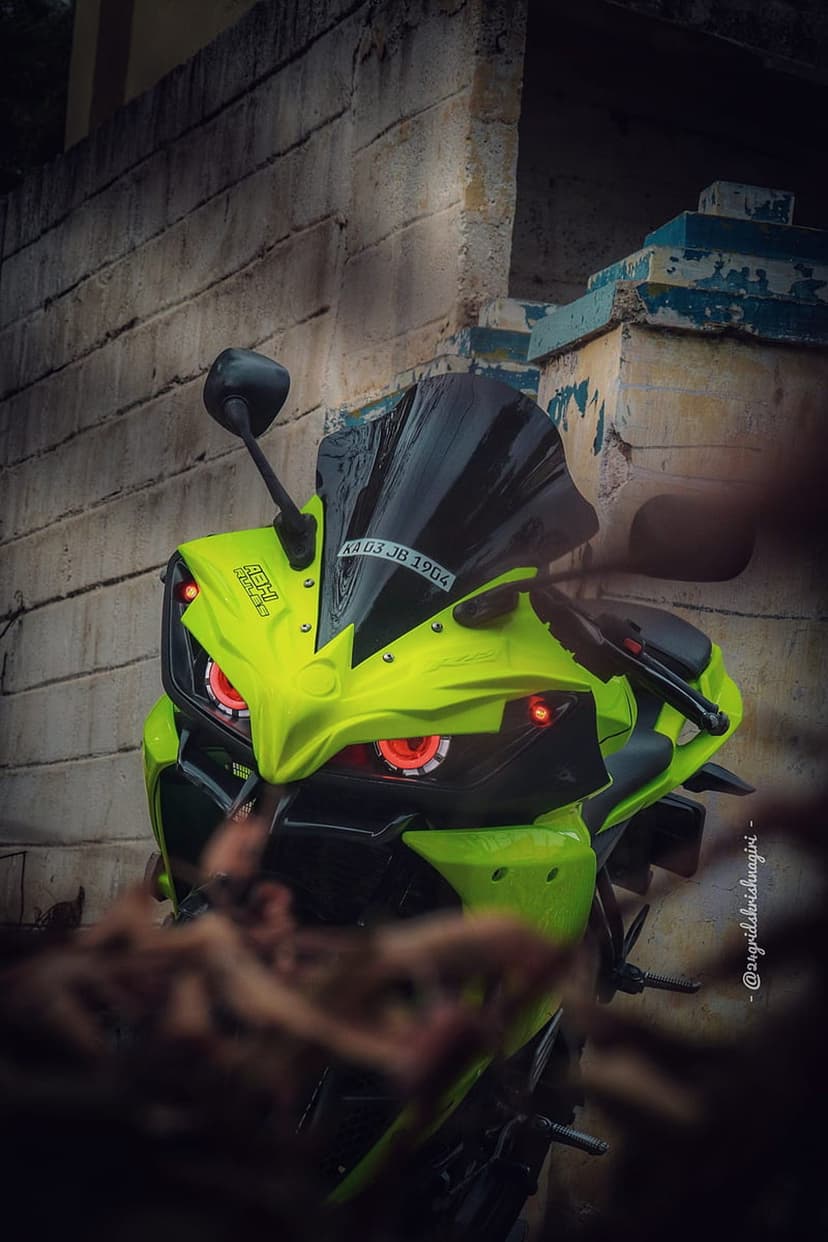 Neon green sport motorcycle featuring glowing red angel eye headlights against a textured urban stone wall.