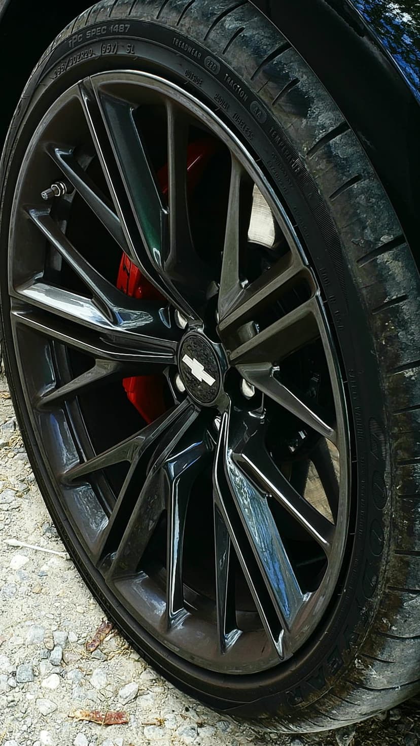 Camaro black multi-spoke wheel with red brake calipers and a Chevrolet bowtie emblem on the center hub.