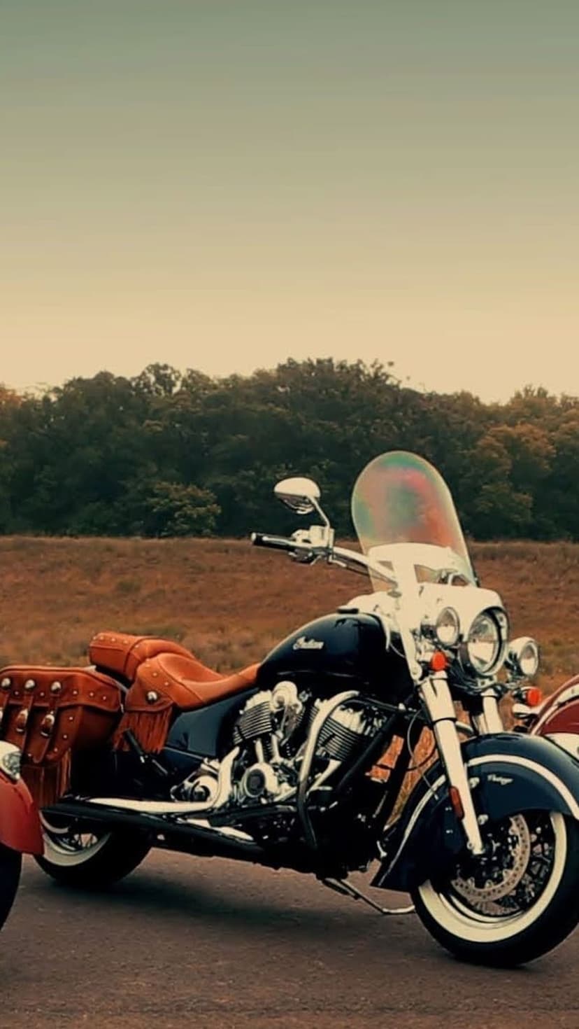 Black Indian motorcycle with brown leather saddlebags parked outdoors against a blurred forest background.