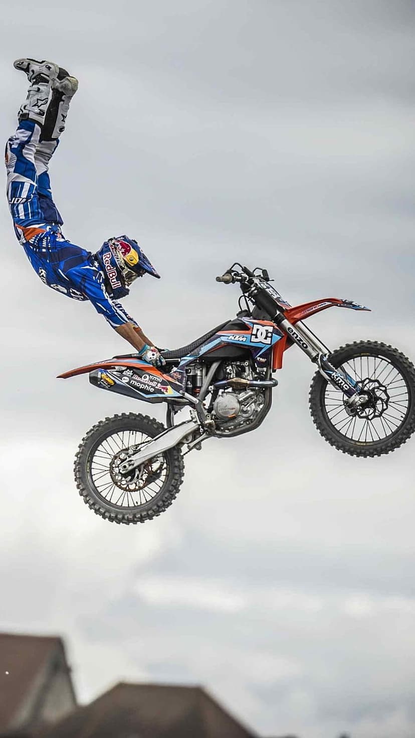 Motocross rider performs a mid-air grab on a KTM dirt bike against a cloudy sky in this vertical action photo.