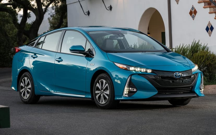Teal Toyota Prius Prime parked on asphalt in front of a white arched building under soft evening light.