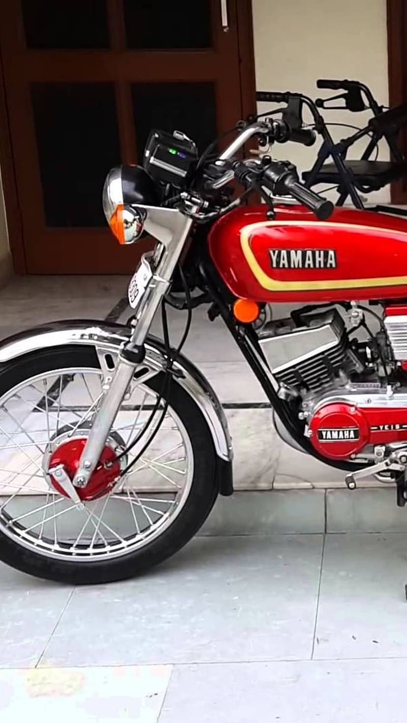 Red Yamaha RX100 motorcycle front view featuring a round chrome headlight, spoked rims, and a vintage engine.