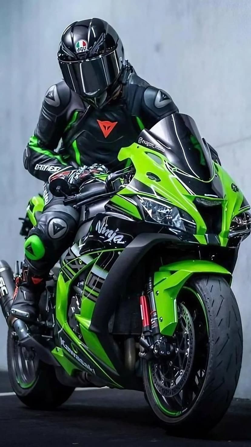 Motorcycle rider in green racing leathers sits on a Kawasaki Ninja with a mirrored helmet visor and sharp fairings.