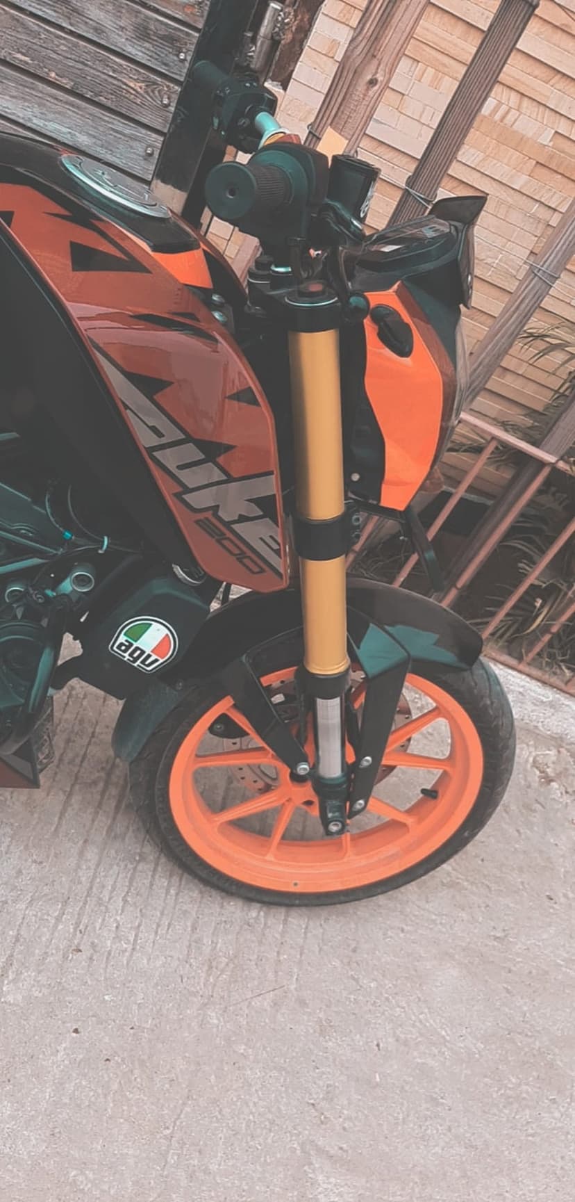KTM Duke motorcycle front wheel with a bright orange rim and golden suspension forks against a concrete surface.