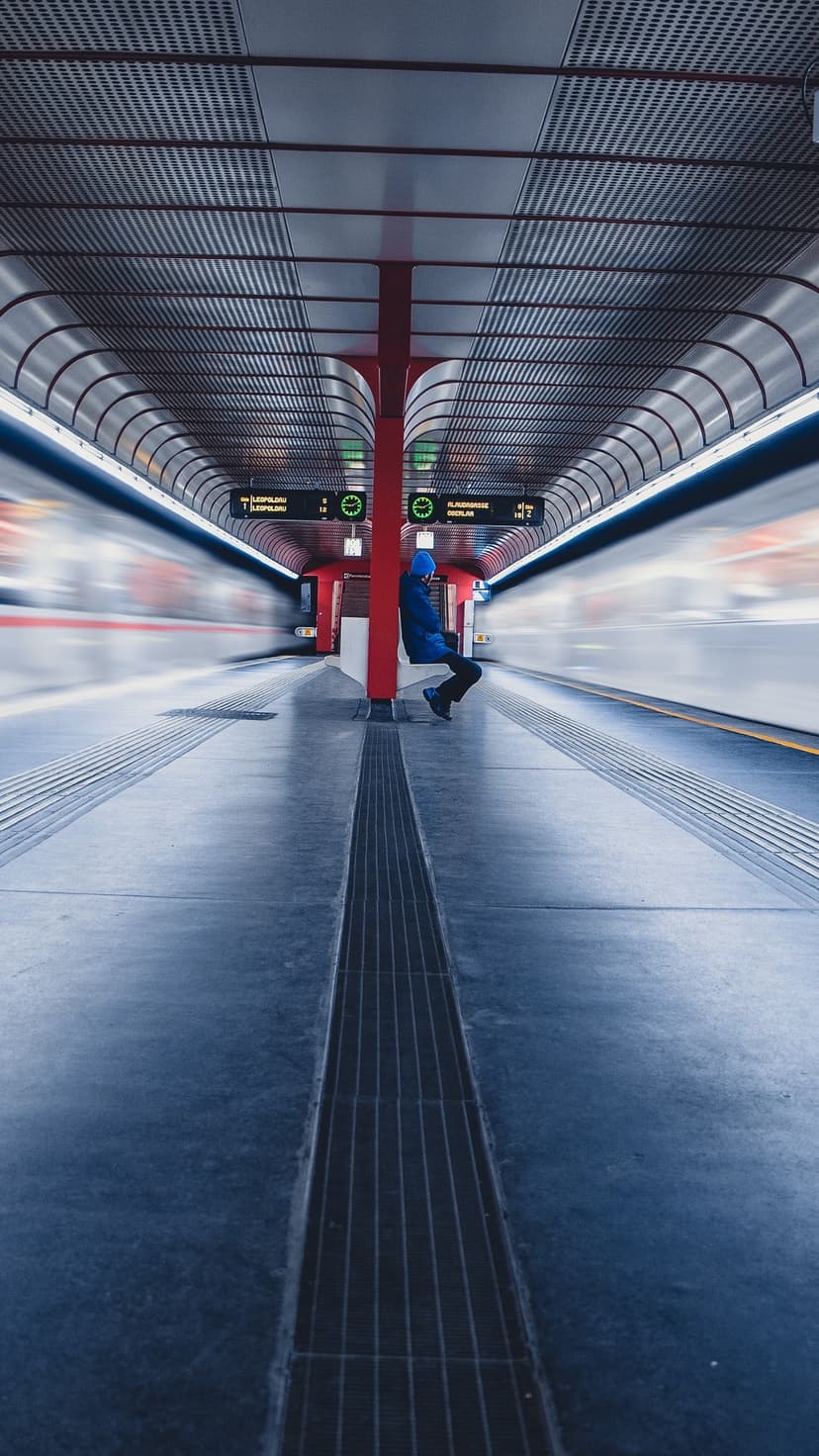 Person in a blue jacket sitting on a subway platform next to long exposure motion streaks of a passing train.