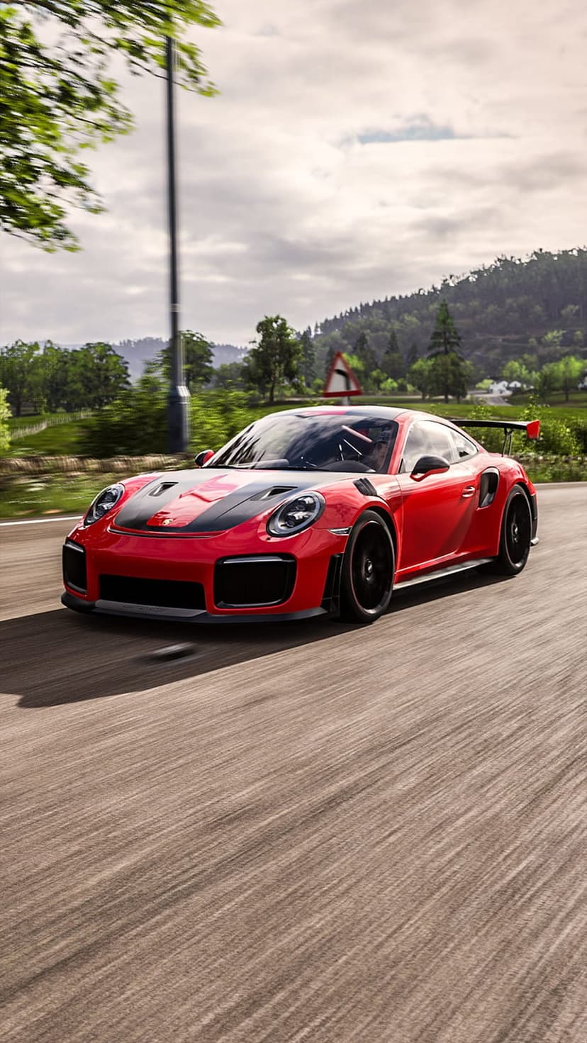 Red Porsche GT2 RS supercar speeding past green trees on a winding road with a cloudy sky in the background.
