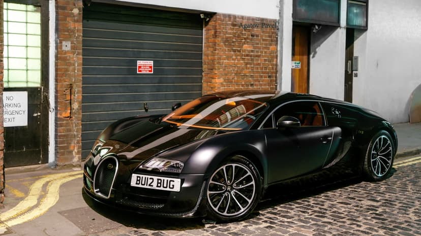 Matte black Bugatti Veyron parked on a cobblestone street at night with glowing orange interior and brick background