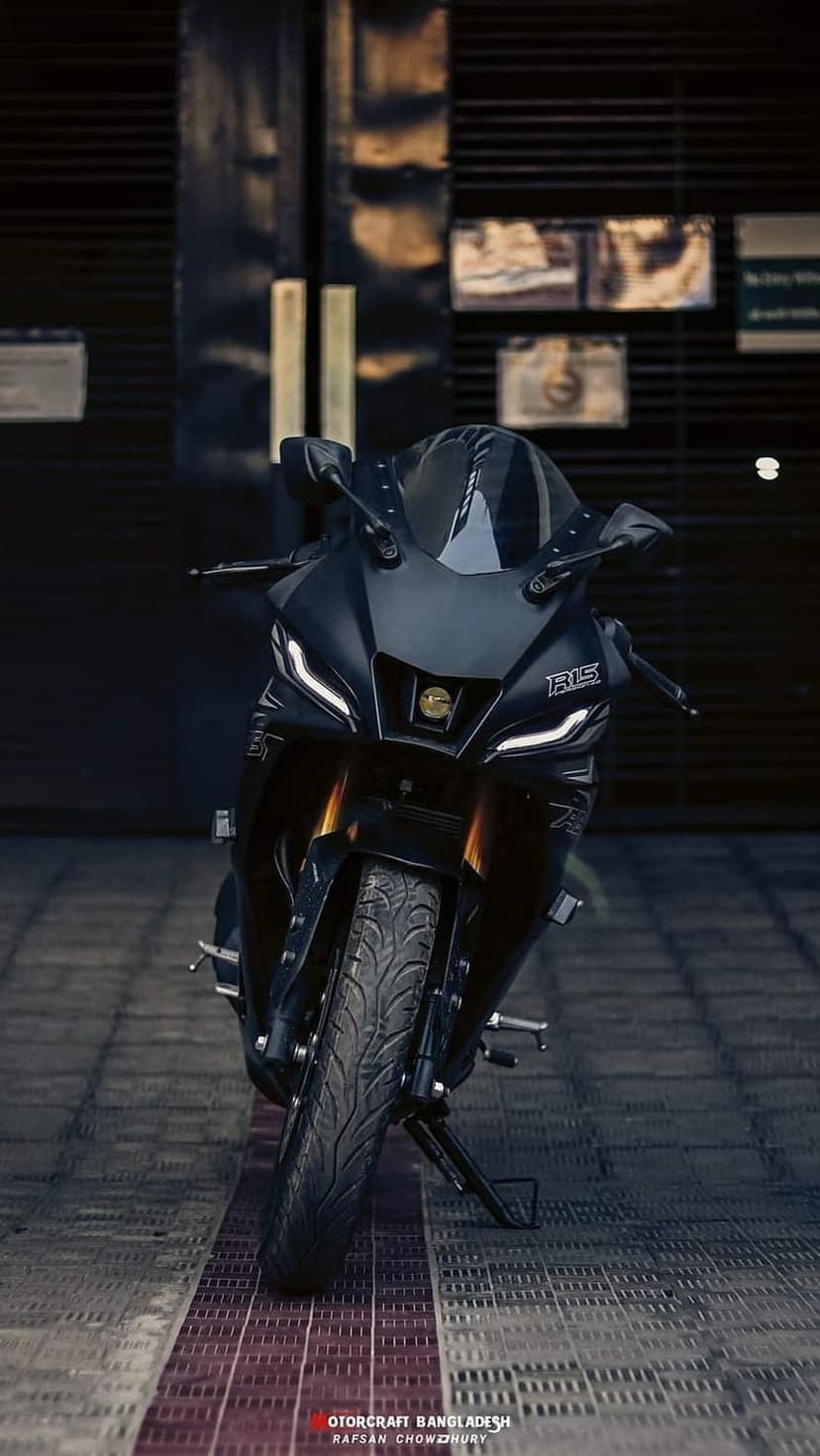 Yamaha R15 motorcycle front view with glowing LED headlights, golden forks, and a black finish in a dark studio.
