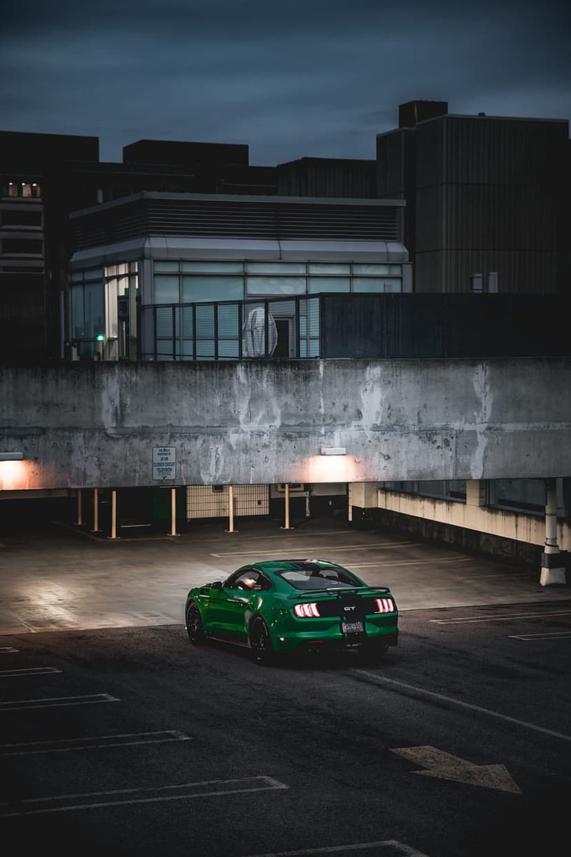Green Mustang GT sports car parked in a shadowed concrete garage with artificial lights reflecting on its paint.