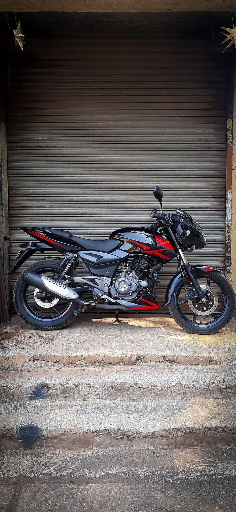 Black sportbike with red accents parked on concrete steps in front of a corrugated metal garage door in an alley.