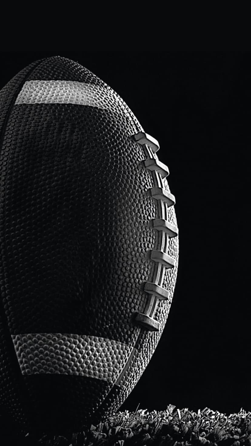 American football with prominent laces sits on artificial turf in a high-contrast black and white close-up shot.