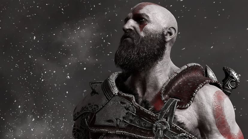 Kratos with a red tattoo and beard stands in falling snow wearing detailed leather and metal armor.
