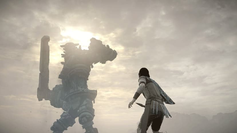 Wander holds a sword while facing a massive stone giant silhouetted against a bright, hazy, cloudy sky.