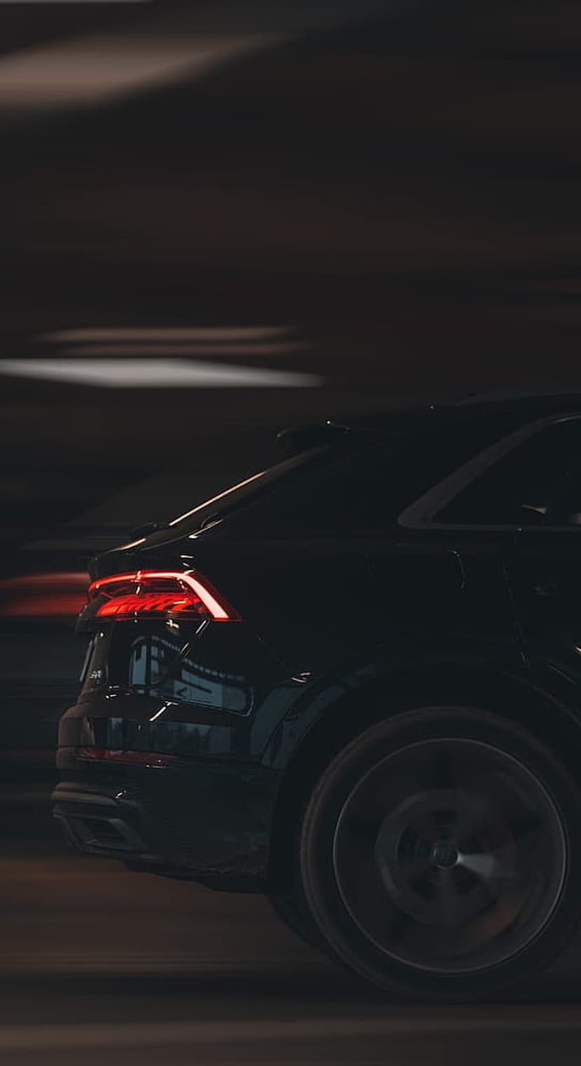 Audi SUV rear LED lights glowing red during night driving with dynamic motion blur against a dark background.