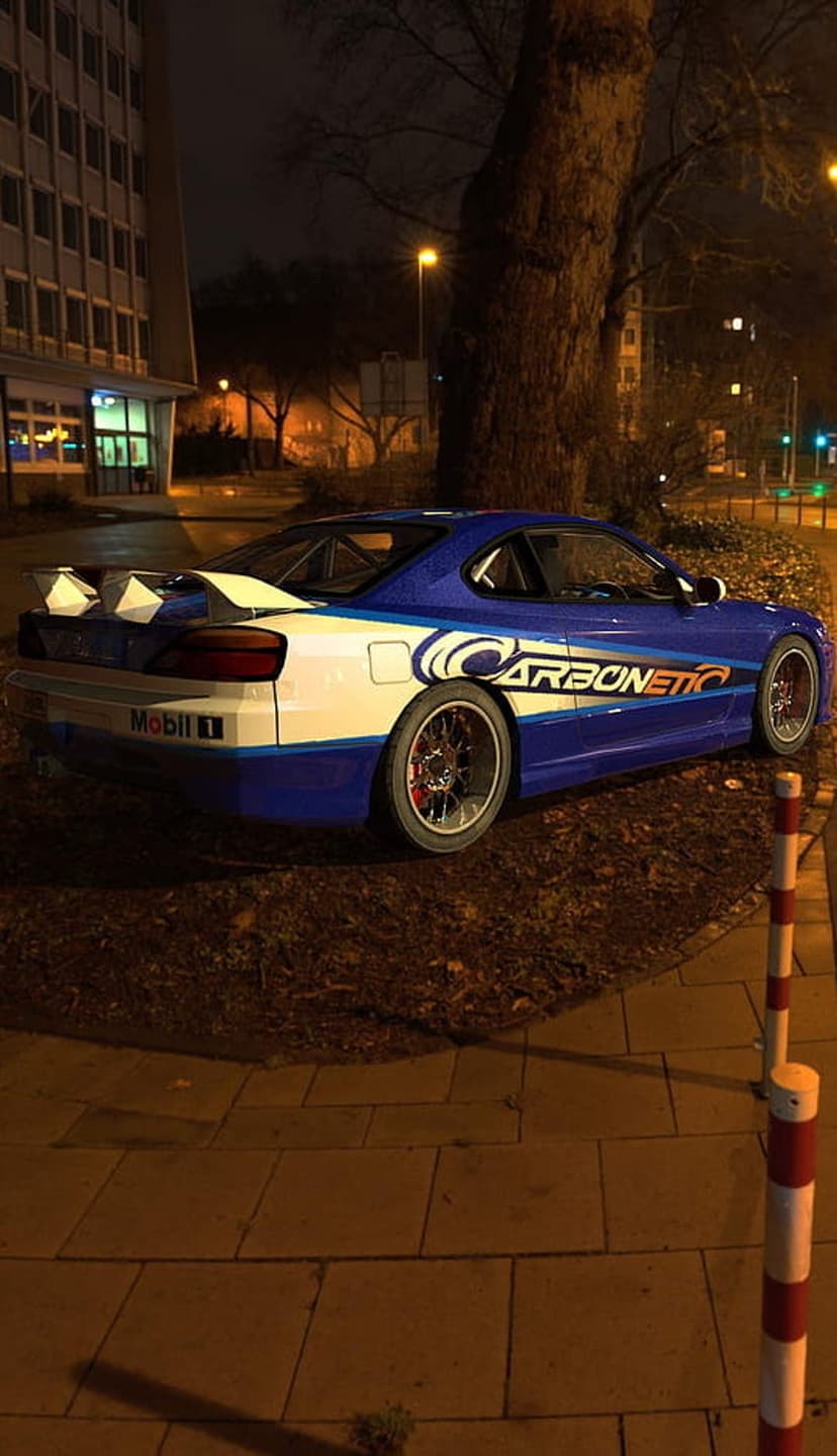 Nissan S15 Silvia sports car in blue and white livery with a large rear spoiler parked on a dark sidewalk.