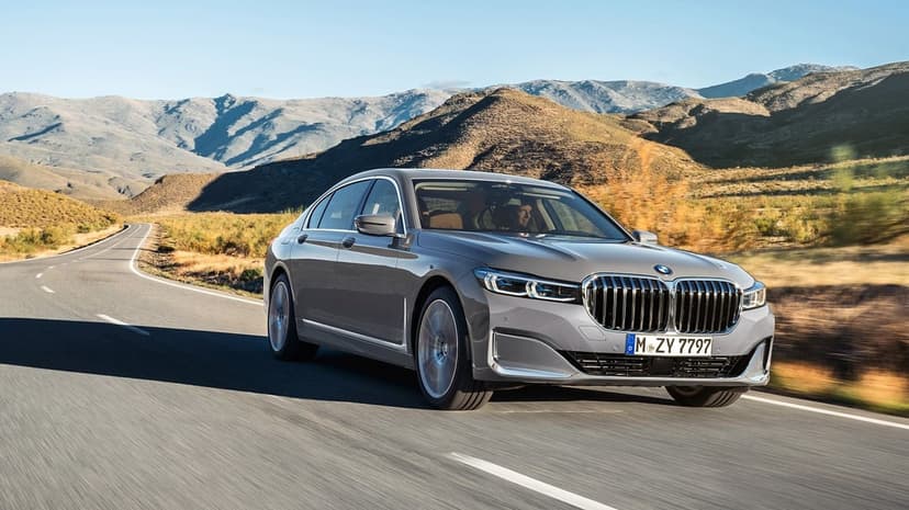 Grey BMW luxury sedan driving fast on a winding mountain road under a clear blue sky in bright daylight.