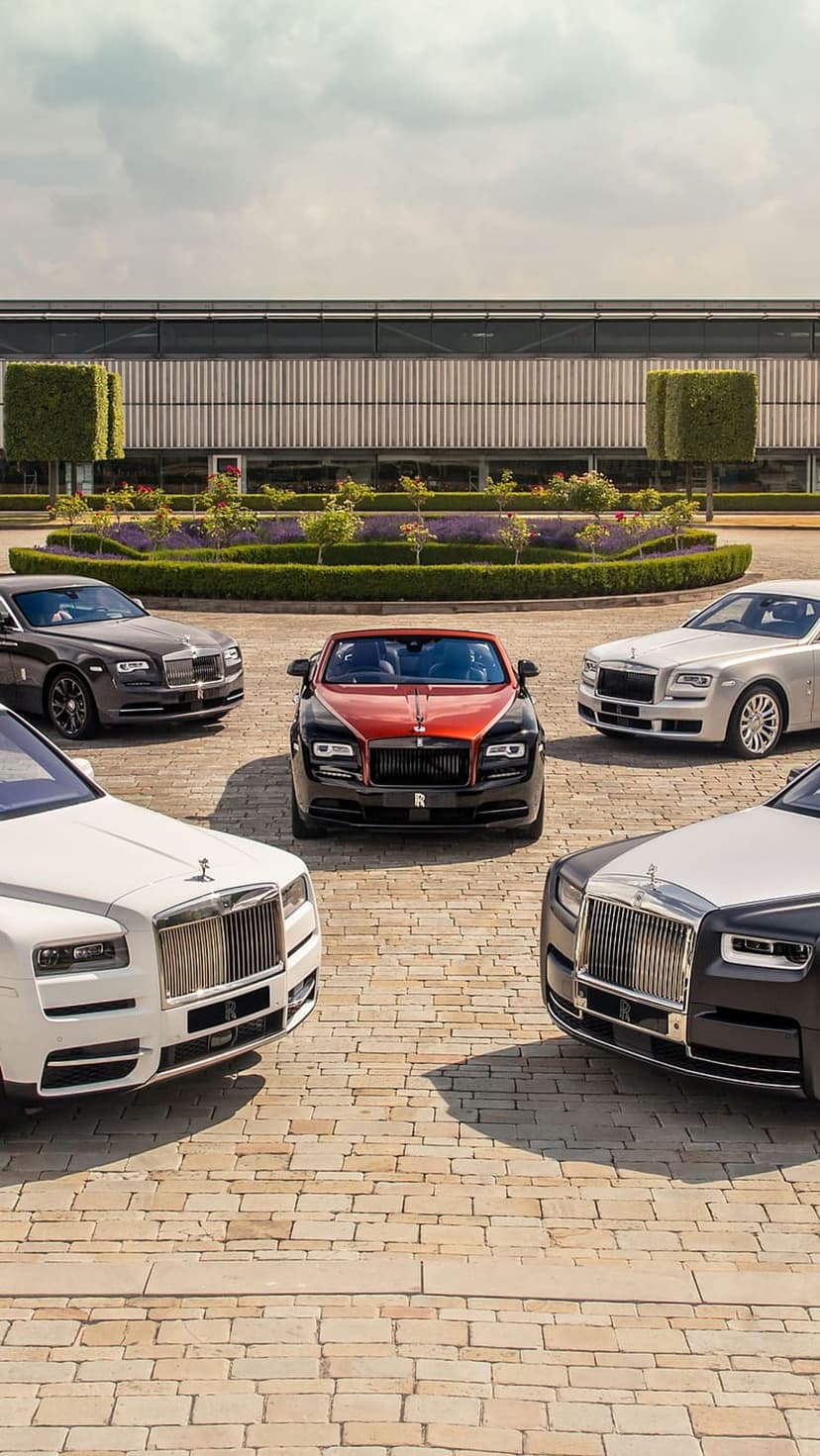 Rolls-Royce luxury cars in black, white, and red parked on a paved driveway in front of a contemporary building.