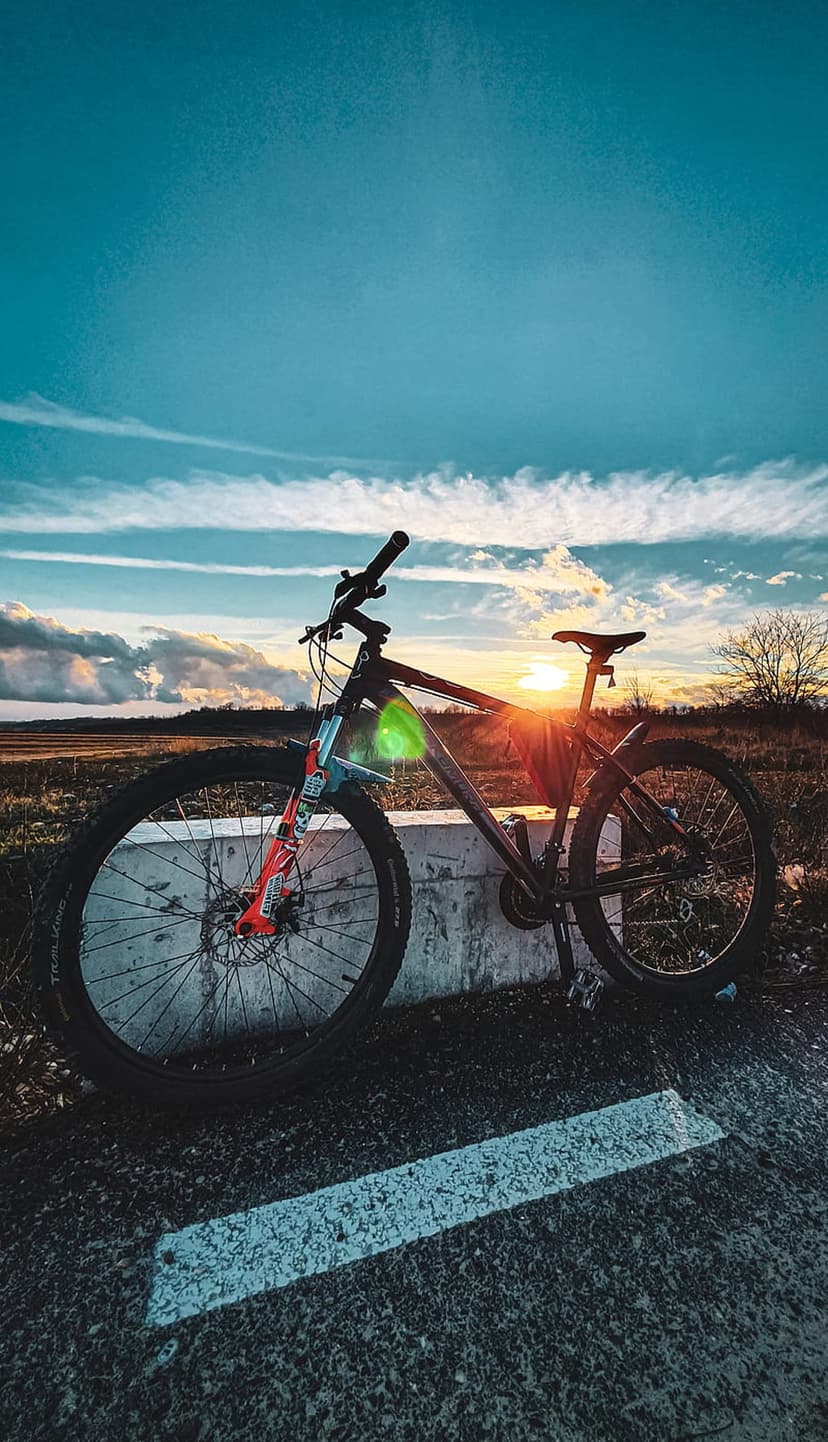 Mountain bike on a roadside barrier overlooking a field during a golden sunset with a prominent sun lens flare.