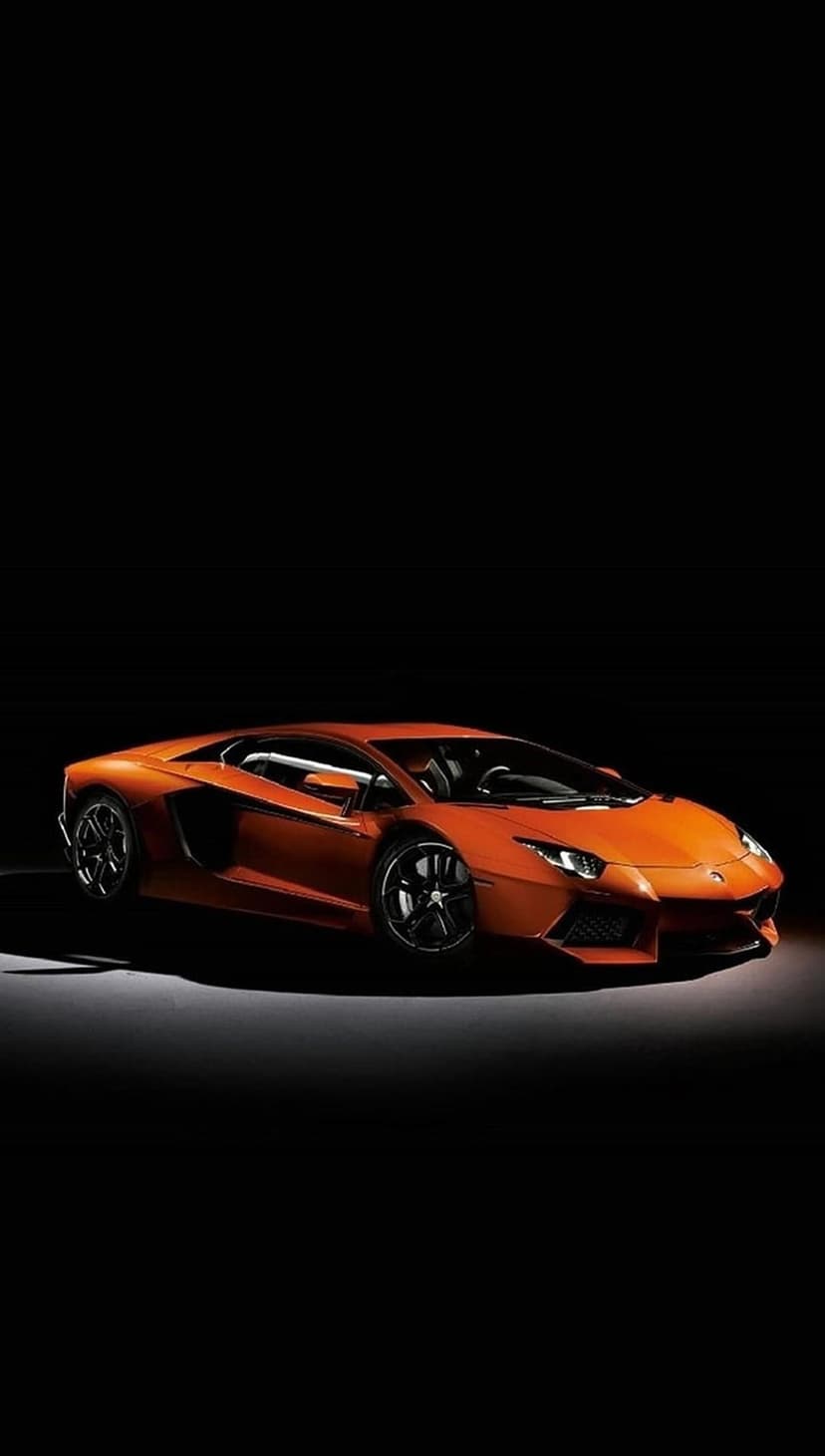 Orange Lamborghini Aventador with aggressive front vents and low-profile stance against a pitch-black backdrop.