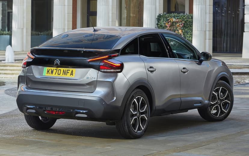 Grey Citroën ë-C4 electric car parked in an urban plaza with glowing red LED taillights and bi-tone alloy wheels.