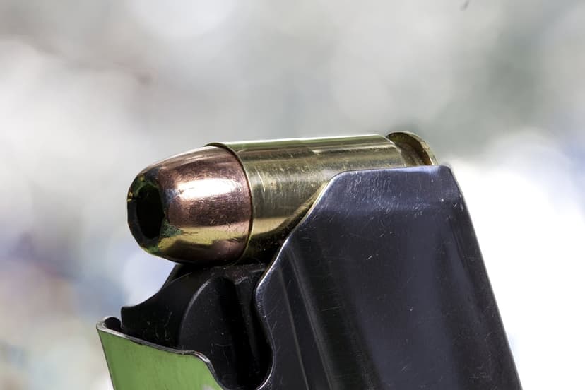 Brass 9mm bullet seated in a black metal magazine with a shallow depth of field and blurred background.