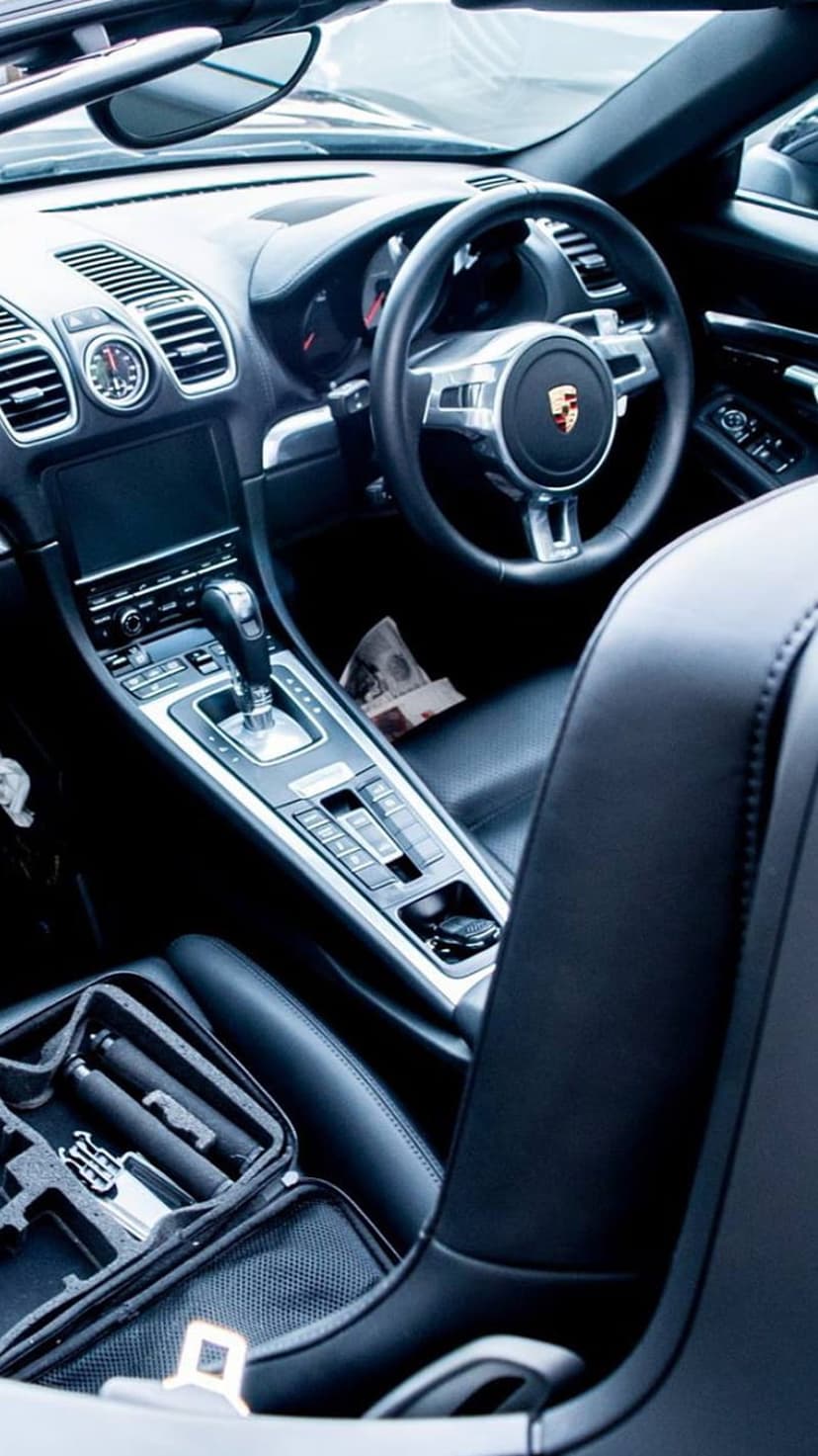 Porsche steering wheel with emblem and glowing dashboard gauges inside a luxury black leather automotive cabin.