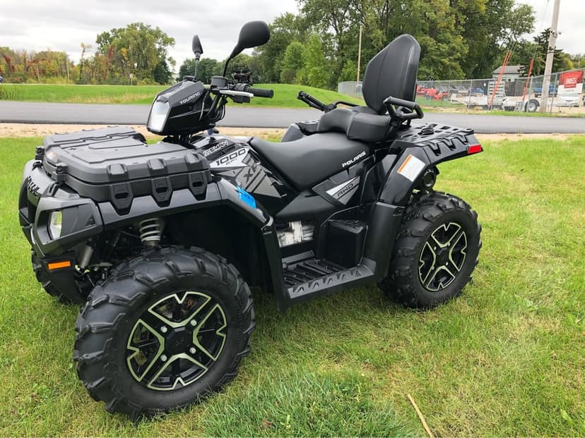 Black Polaris Sportsman Touring ATV with off-road tires parked on a green field under an overcast sky.