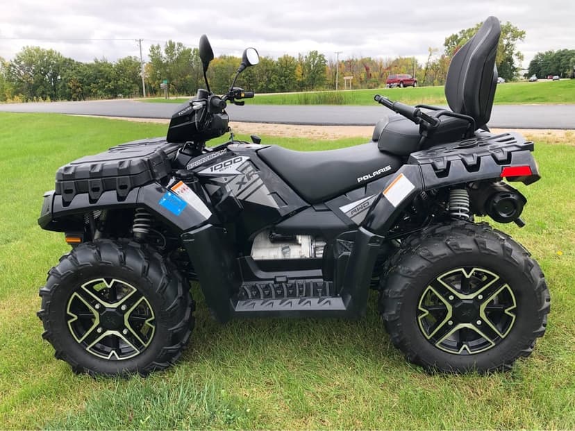 Black Polaris Sportsman 1000 XP Touring ATV with lime green wheel accents parked on a green grassy field.
