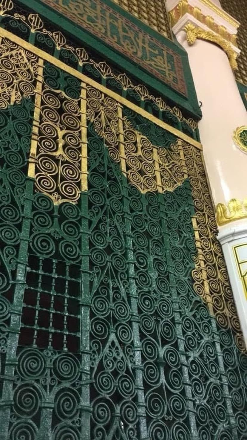 Ornate green metal grilles with gold Arabic calligraphy and a cream pillar showcase Islamic architectural detail.
