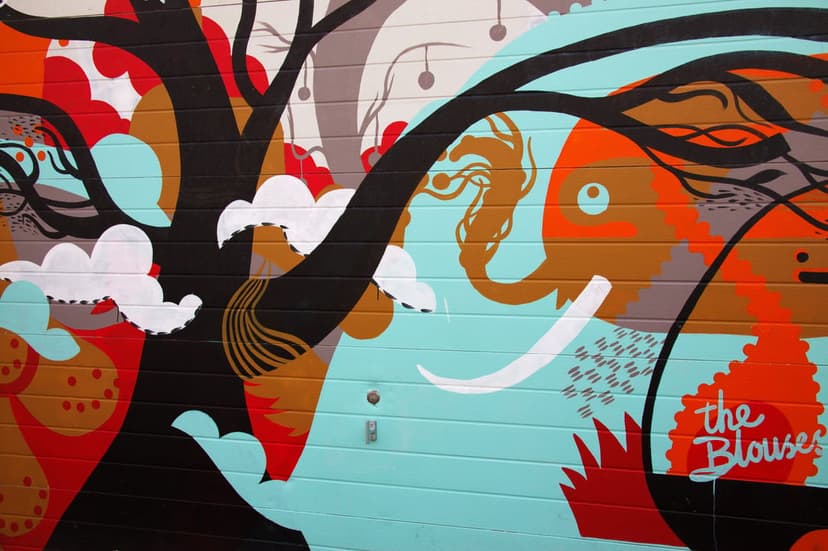 Stylized orange and teal elephant mural painted on a garage door with abstract trees and fluffy cloud shapes.
