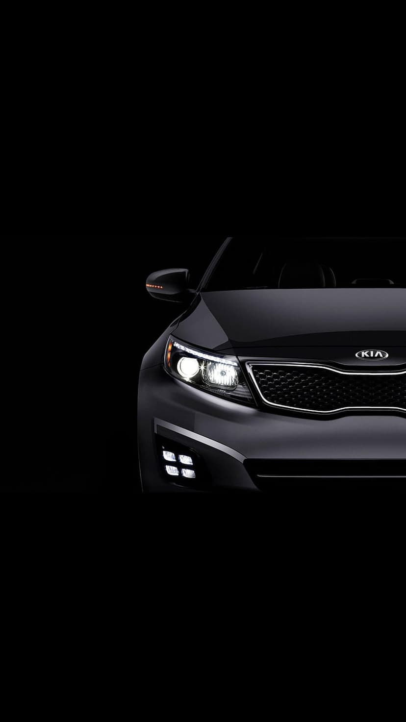 Black Kia car headlights and front grille glowing against a dark studio background with sharp reflections.