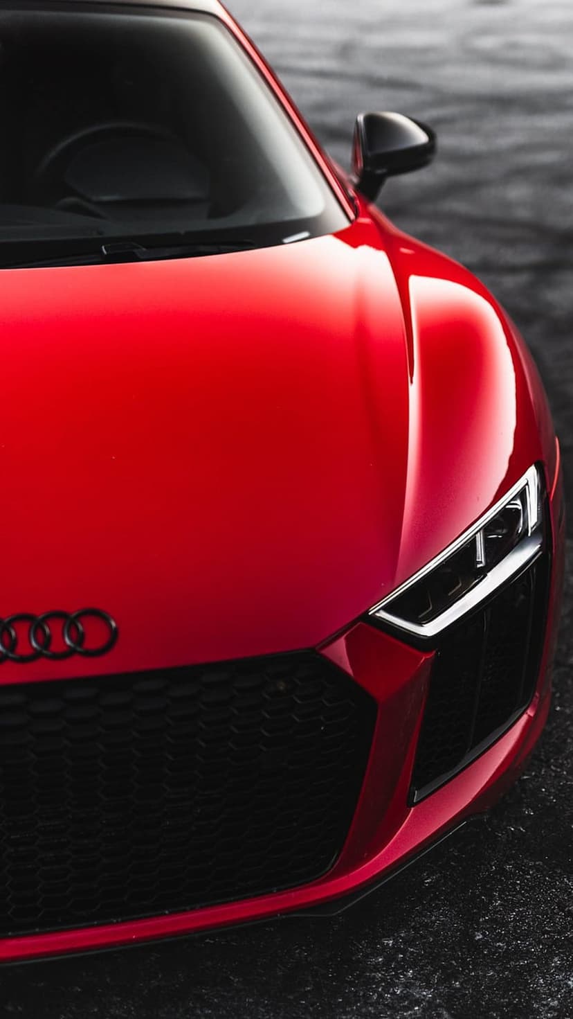 Red Audi R8 front grille and sharp LED headlight detail featuring the chrome four-ring emblem and honeycomb mesh.