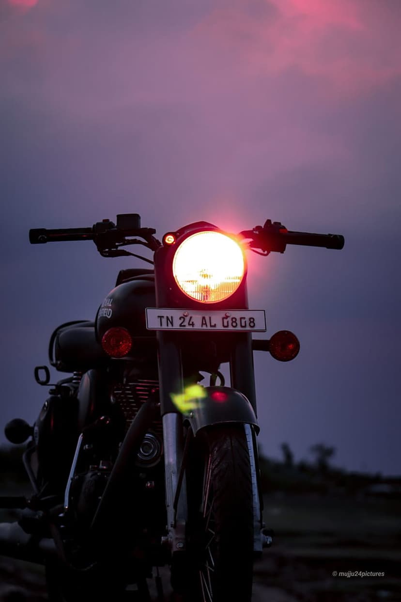 Royal Enfield motorcycle headlight glowing at dusk with visible license plate TN 24 AL 0808 against a dark sky.