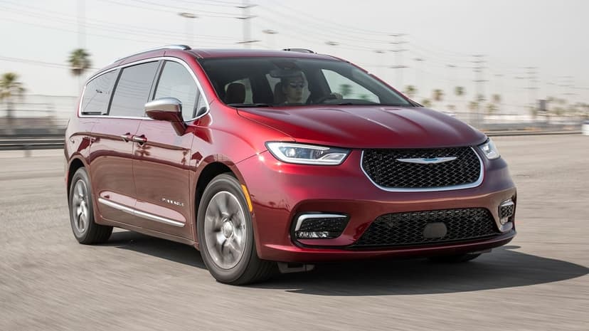 Red Chrysler Pacifica Pinnacle minivan driving on a sunlit paved track with visible motion blur on the wheels.