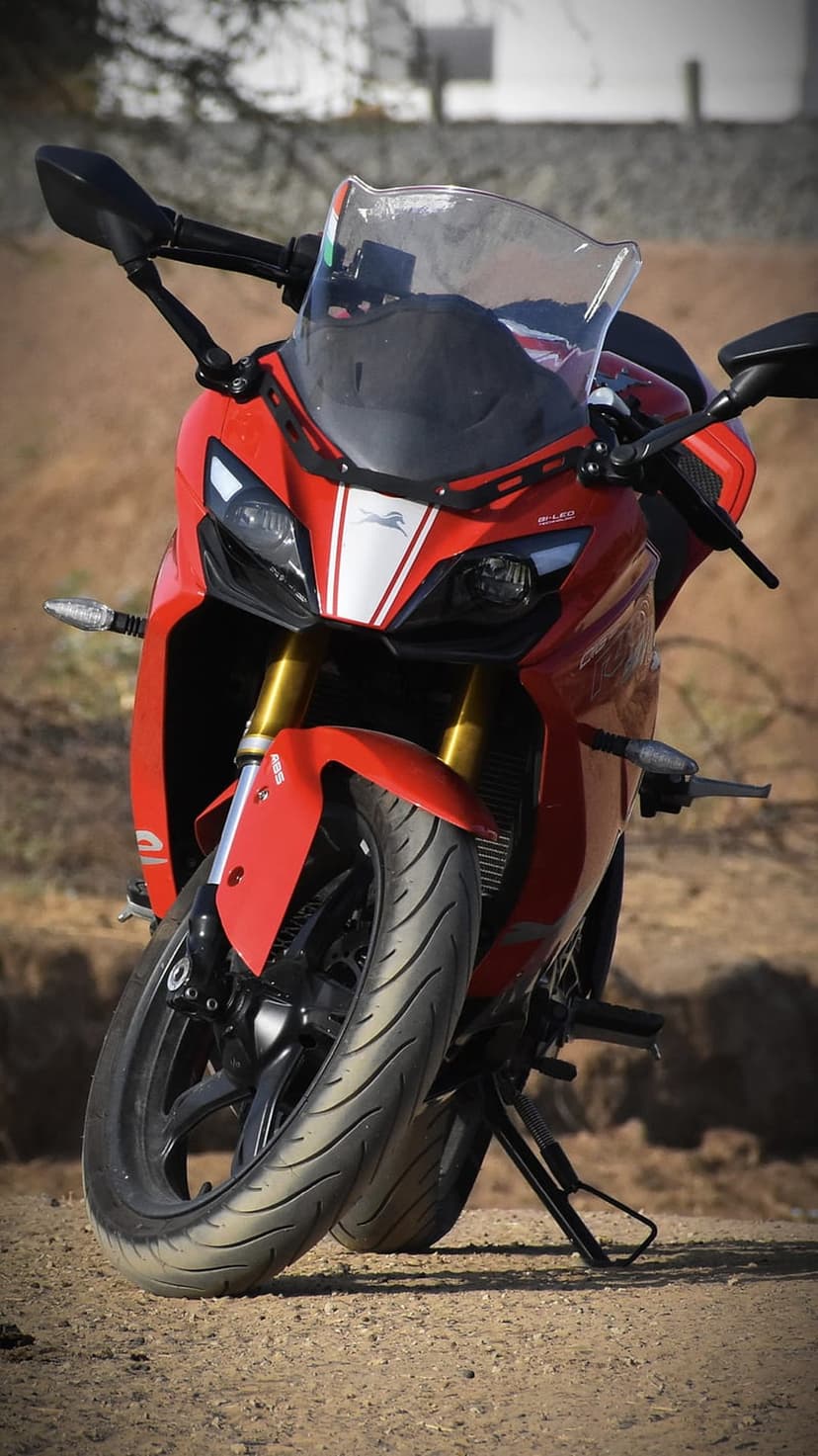 Red sportbike front view featuring sharp headlights, racing stripes, and front tire on a rustic dirt path.