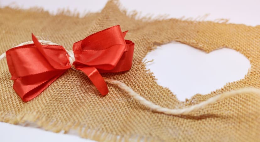 Red satin bow tied on burlap fabric featuring a heart cutout and a thin natural fiber string.