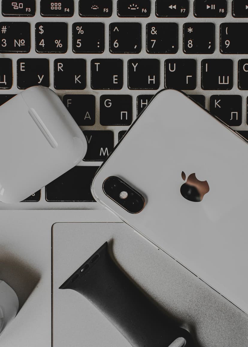 iPhone, wireless earbud case, and black watch band arranged on a gray laptop keyboard in a top-down view.