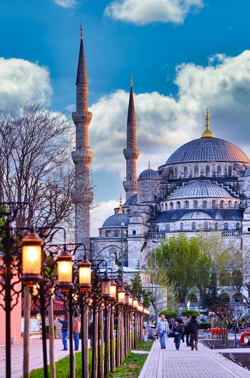 Sultan Ahmed Mosque minarets and domes silhouetted against a purple dusk sky behind glowing outdoor lanterns.