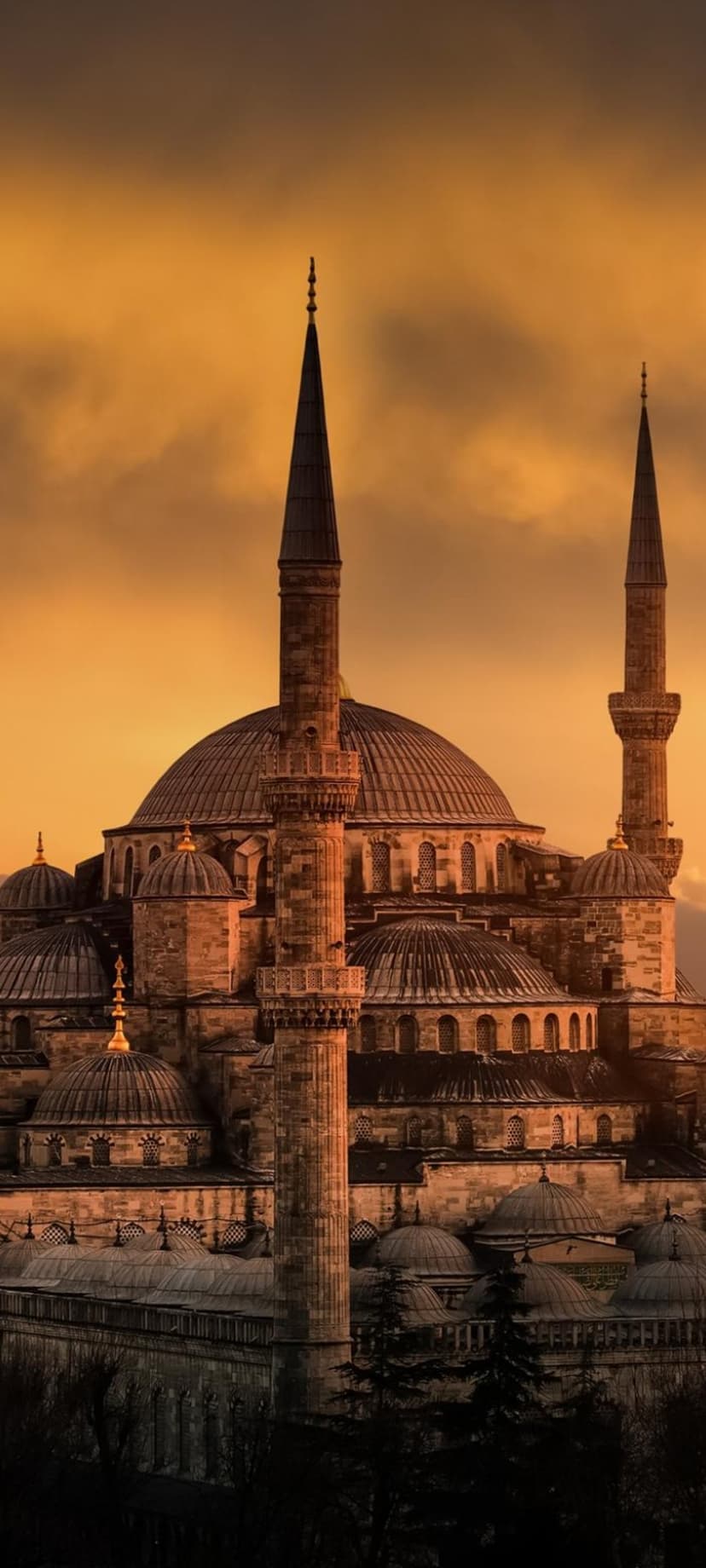 Sultan Ahmed Mosque minarets and domes silhouetted against a vibrant orange and yellow sunset sky in Istanbul.