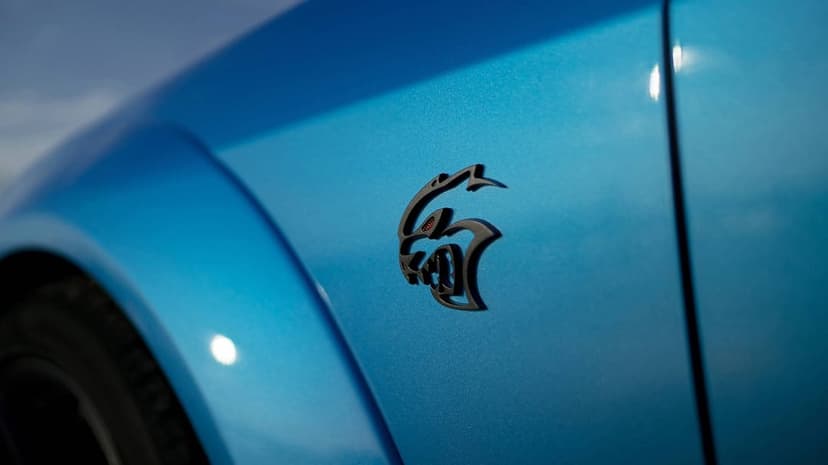Black SRT Hellcat logo on metallic blue car paint with shallow depth of field and soft outdoor lighting.