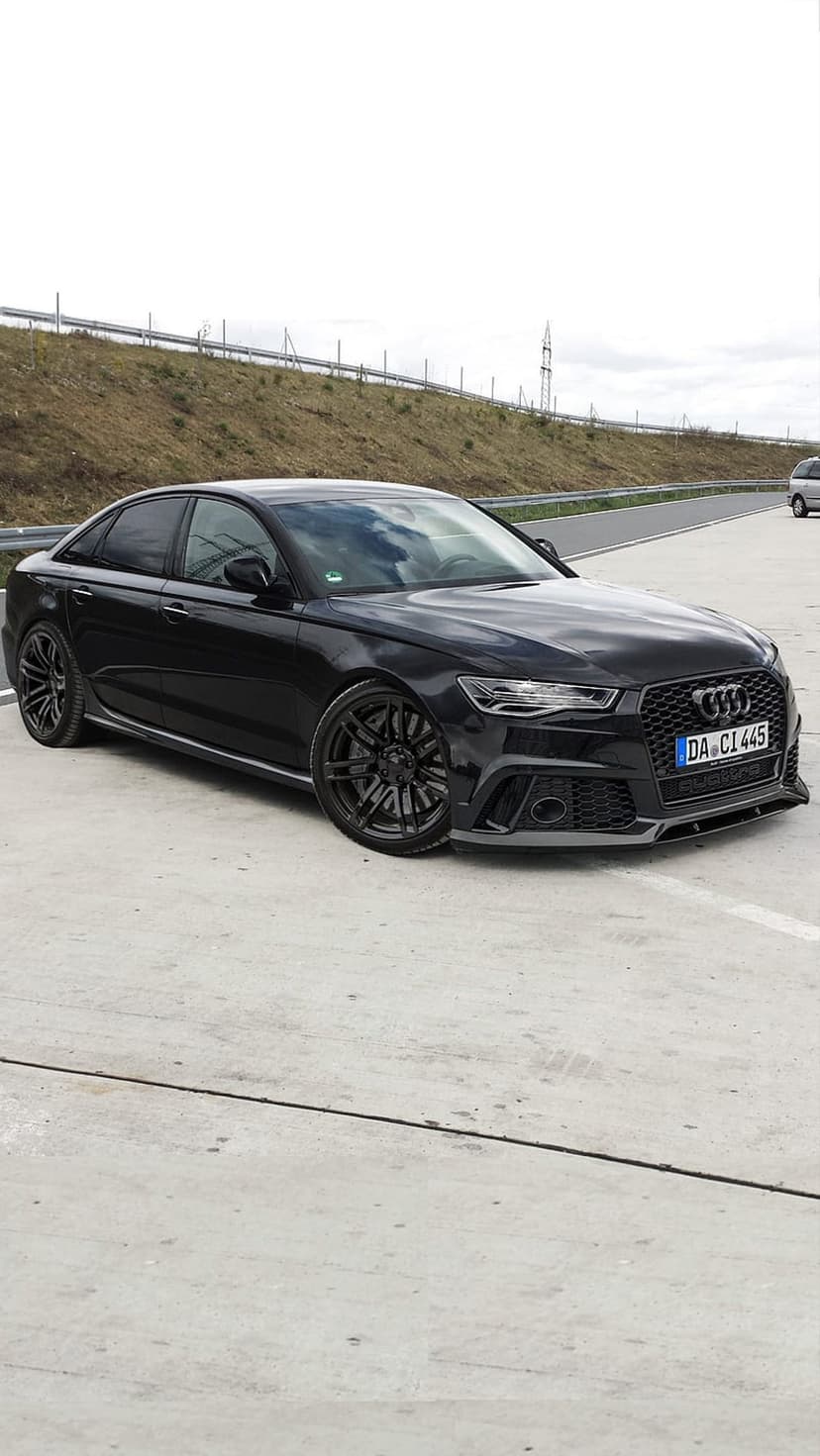 Black Audi RS6 Avant wagon with dark rims parked on concrete under a cloudy sky during an overcast day.