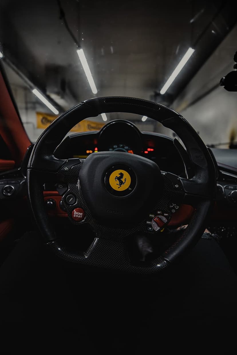 Ferrari steering wheel featuring a yellow prancing horse crest and a red ignition button inside a dark supercar.